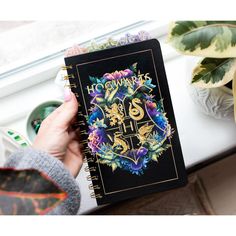 a person holding a notebook with the harry potter crest on it, next to potted plants