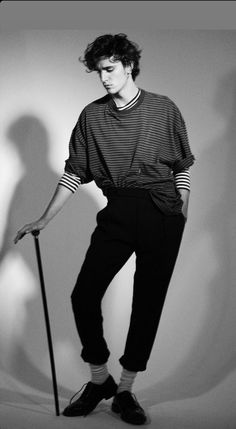 a man with a cane standing in front of a white wall wearing black pants and a striped shirt