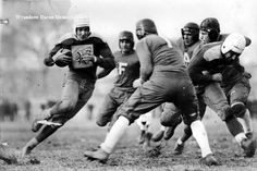 an old black and white photo of a football player running with the ball in his hands