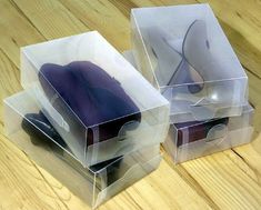 three clear boxes with purple items in them on a wooden surface, one is empty