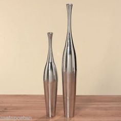 two silver vases sitting on top of a wooden table next to eachother