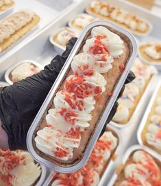 a person holding up a container with some food in it and other trays full of pastries