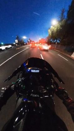 a motorcycle is driving down the road at night with other cars in the back ground