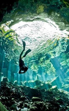 a person swimming in an underwater cave with sunlight streaming through the water's surface