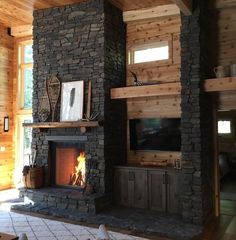 a living room with a fire place and stone fireplace in the center, surrounded by wood paneling