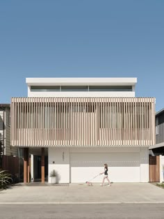 a woman walking her dog in front of a large house with wooden slats on the roof