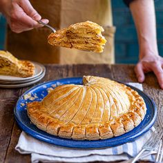 a person holding a piece of food over a pie on a blue plate with a fork