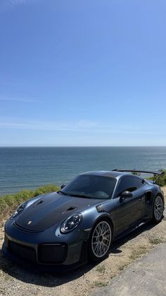 a black sports car parked on the side of a road next to the ocean and grass