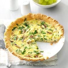 a quiche on a plate with a piece missing from it and a bowl of grapes in the background