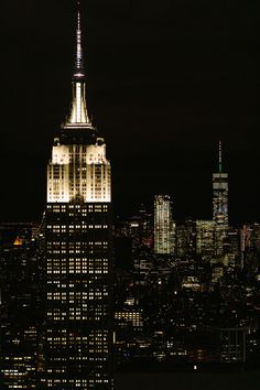 the empire building is lit up at night in new york city, ny with skyscrapers visible