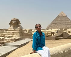 a woman is sitting on a ledge in front of the pyramids and sphinxs