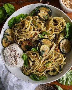 a white bowl filled with pasta and zucchini on top of a wooden table