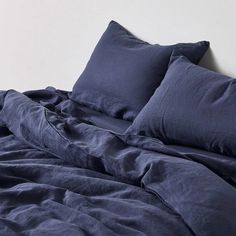 an unmade bed with dark blue linens and pillows on top of the bed