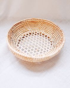 a wicker bowl sitting on top of a white cloth covered table with a light colored background