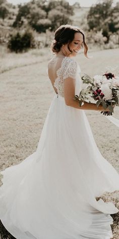 a woman in a white dress holding a bouquet and looking at the camera while standing in a field