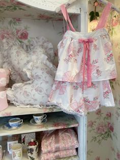 a dollhouse closet with pink and white floral wallpaper, bedding and accessories