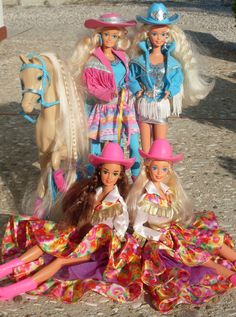 four barbie dolls sitting on the ground next to each other with horses in the background