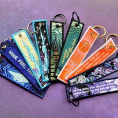 six keychains with different designs on them sitting next to each other in front of a purple background