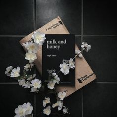 the book milk and honey is next to some white flowers on a black tile floor