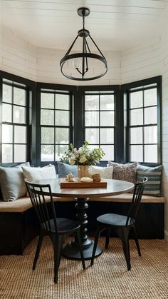 a dining room table with four chairs and a bench in front of three large windows