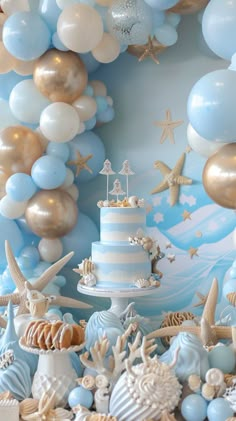 a blue and white cake surrounded by balloons, seashells and starfishes