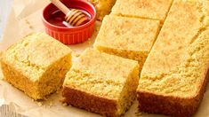 several pieces of cake sitting on top of a piece of wax paper next to a bowl of honey