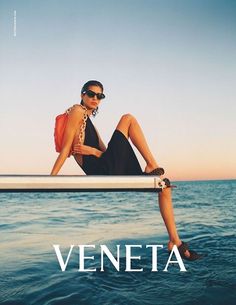 a woman sitting on top of a boat next to the ocean with her legs crossed