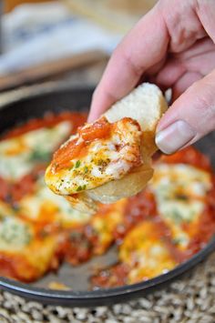 a hand holding a piece of bread with sauce and cheese on it in a pan