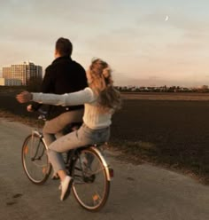 a man and woman riding on the back of a bike down a road next to a field