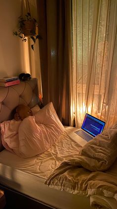 a laptop computer sitting on top of a bed next to a window with sheer curtains