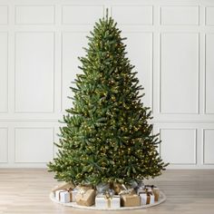 a christmas tree with presents under it on a wooden floor in front of a white wall