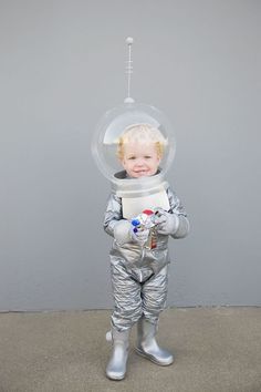 a small child wearing an astronaut suit and holding a toy in his hand while standing next to a gray wall