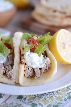 two tacos with meat, lettuce and tomatoes on them sitting on a plate