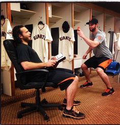 a man sitting in a chair reading a book next to another man wearing black shoes