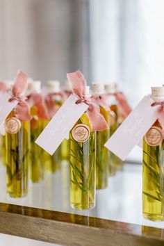 several small bottles filled with green liquid and tied with pink ribbon, each containing an individual's initials