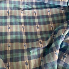 a green and blue checkered shirt with cactus designs on it's chest, sitting on a bed