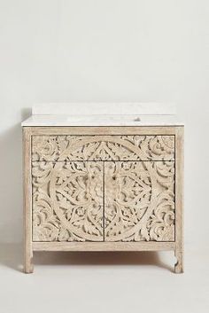 a wooden cabinet with marble top and carvings on the front, sitting against a white wall