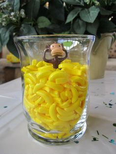 a glass vase filled with yellow pasta noodles and a monkey figurine on top