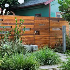 a wooden fence in front of a house with plants and rocks on the ground next to it