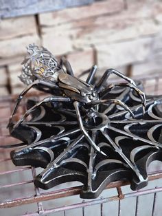 a spider figurine sitting on top of a piece of metal in front of a brick wall