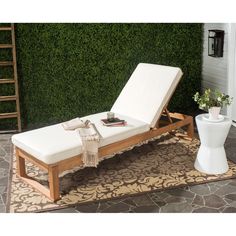 a white lounge chair sitting on top of a rug next to a wall covered in greenery