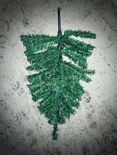 a green plant hanging from a hook on a concrete wall in the shape of a leaf