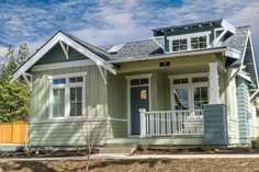 a small green house with white trim on the front porch and two large windows in the back