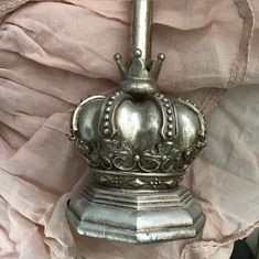 a metal crown is sitting on top of a white cloth covered tablecloth, next to a pink curtain