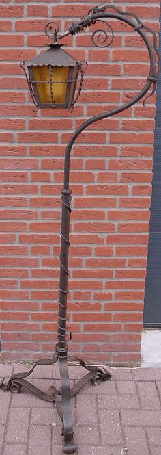 an old fashioned street lamp on the sidewalk next to a brick wall in front of a building