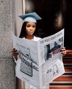 a woman wearing a graduation cap and gown reading a newspaper