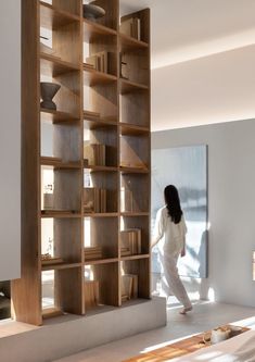 a woman walking past a book shelf in a living room with white walls and flooring