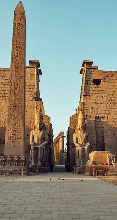 the entrance to an ancient egyptian city with statues and obelisk on either side