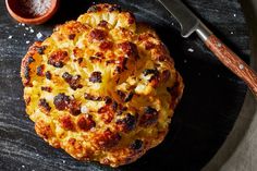 a pizza sitting on top of a black plate next to a knife and bowl filled with condiments