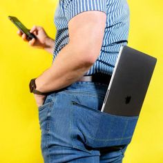 a man holding a laptop and cell phone in his back pocket while standing against a yellow background